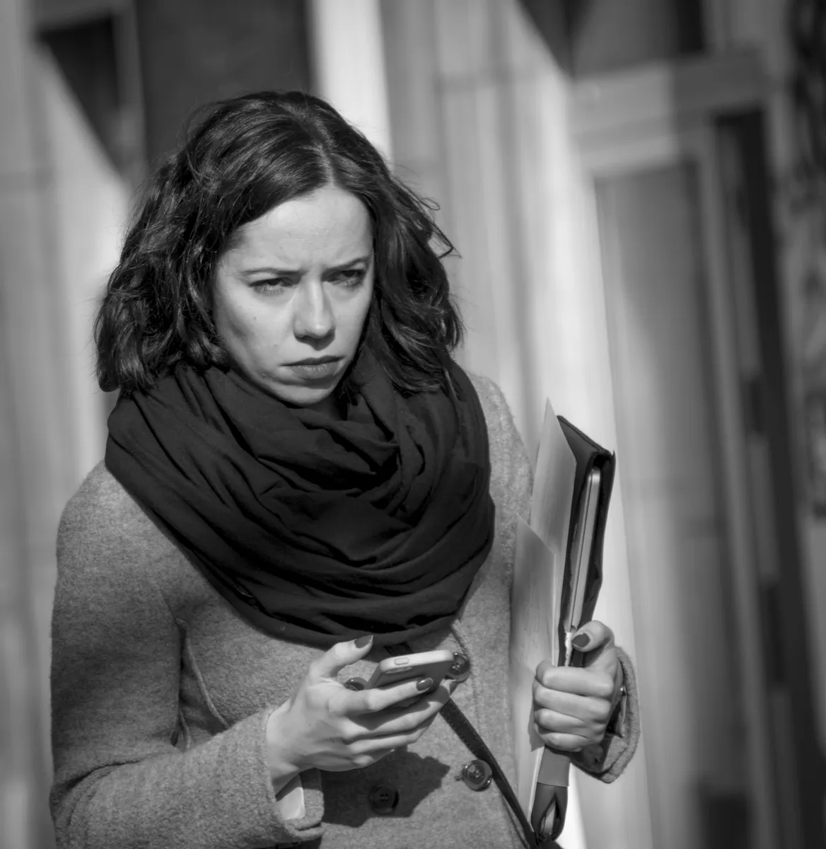 Woman in a scarf checking her phone while holding a folder